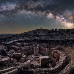 Panoramski noćni pogled na Göbekli Tepe, drevni arheološki lokalitet s kružnim kamenim strukturama i T-stupovima, pod zvjezdanim nebom i Mliječnom stazom.