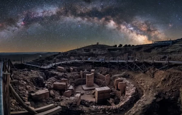 Panoramski noćni pogled na Göbekli Tepe, drevni arheološki lokalitet s kružnim kamenim strukturama i T-stupovima, pod zvjezdanim nebom i Mliječnom stazom.